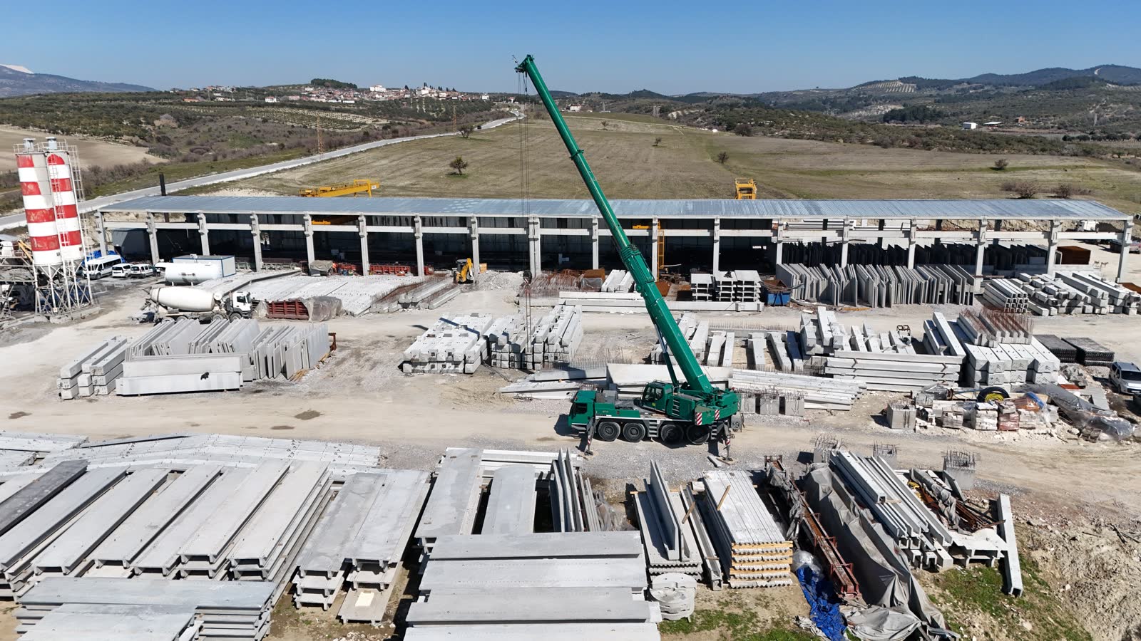 Logo Beton üretim tesisi — havadan geniş açı: üretim holü, portal vinçler ve istiflenmiş hazır betonarme elemanlar